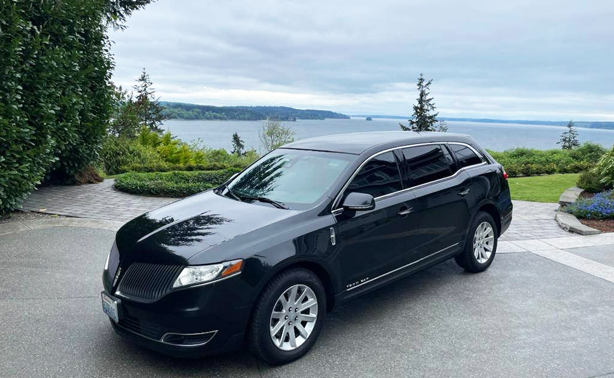 Starline’s black Lincoln Town Car parked on a waterfront driveway picking up a passenger who needs help with luggage, wheelchairs, and airline escorts.