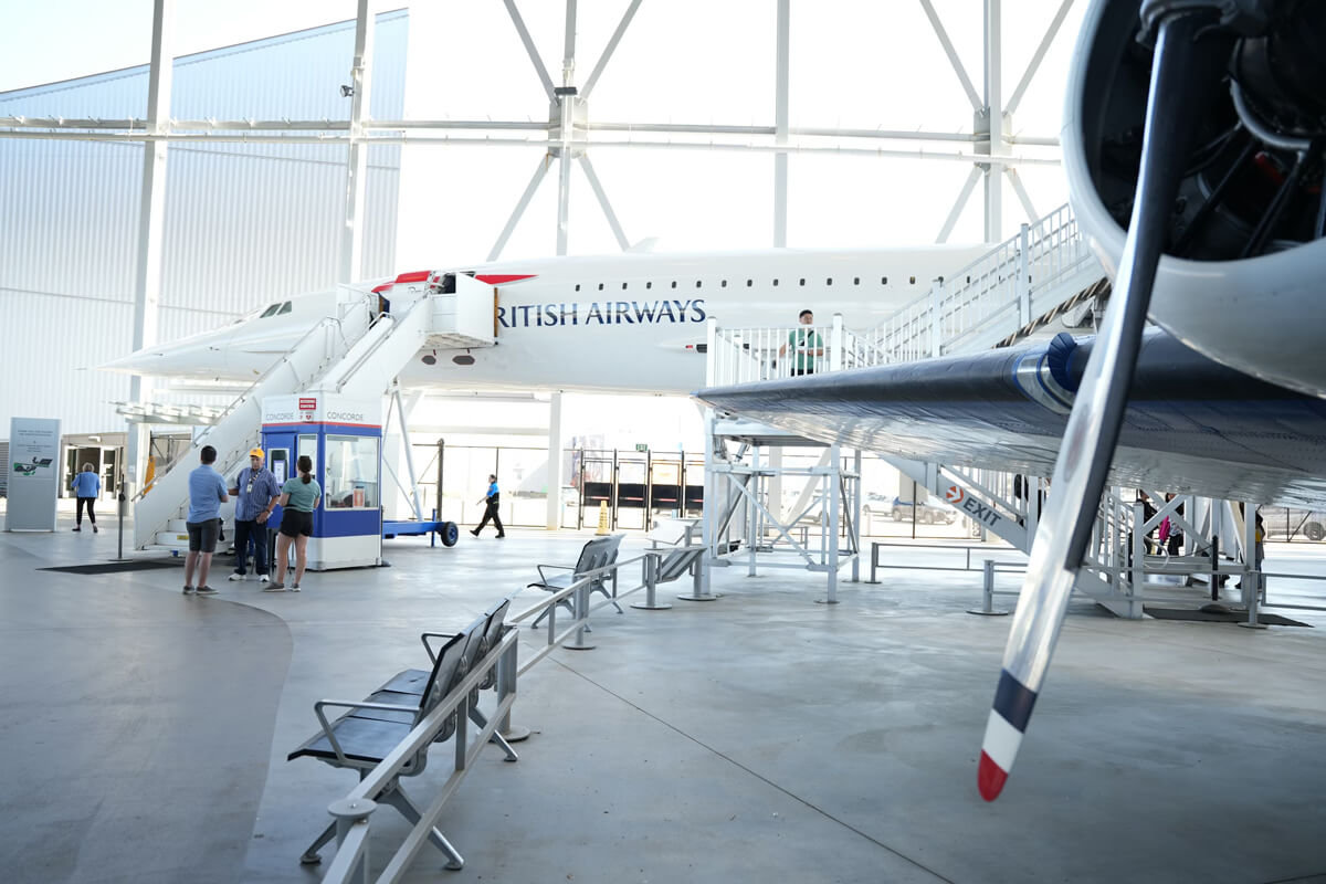 Visitors exploring the British Airways Concorde exhibit inside the Museum of Flight in Seattle, with the aircraft displayed indoors and accessible by stairway.
