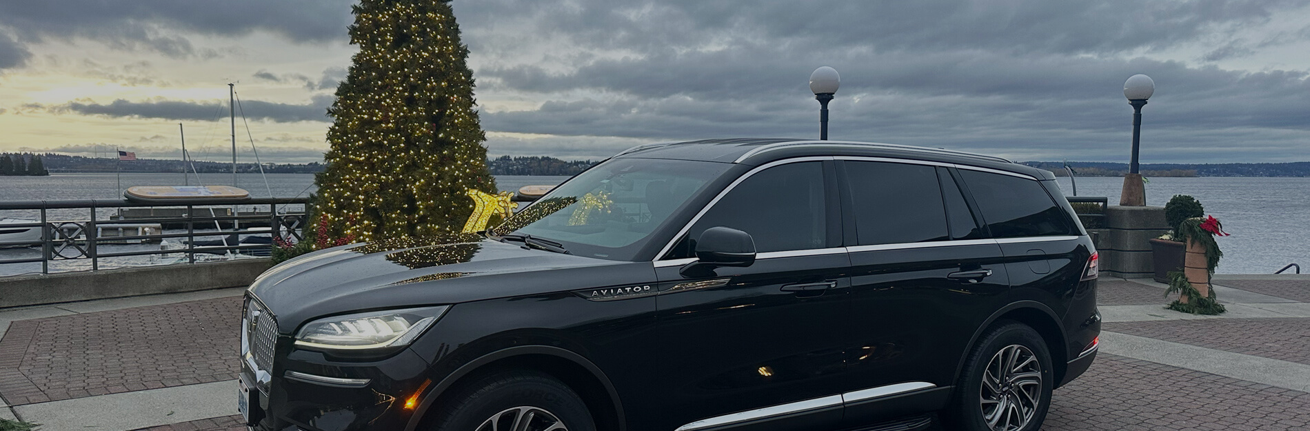 Black Lincoln Aviator SUV by the waterfront in Kirkland, decorated for the holidays with a lit Christmas tree—Starline private chauffeur service in Seattle.
