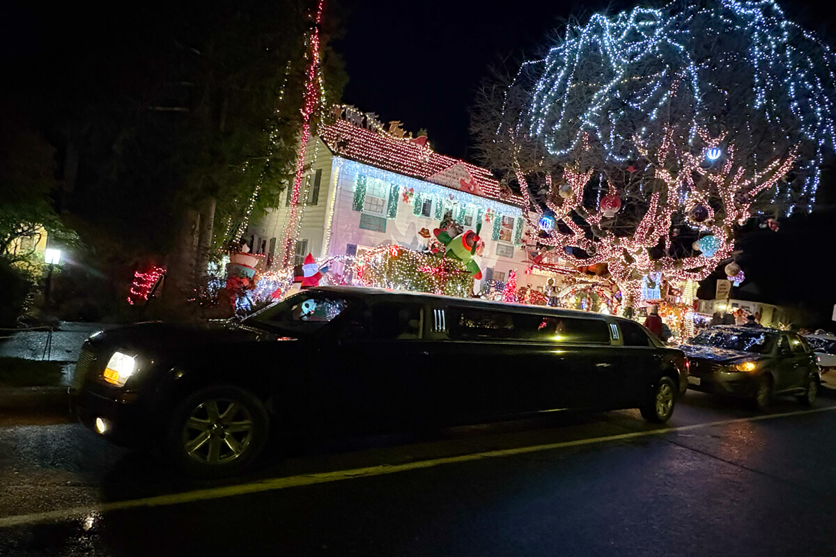 Starline's black stretch limousine driving through a Seattle neighborhood decorated with festive Christmas lights during a holiday light tour.