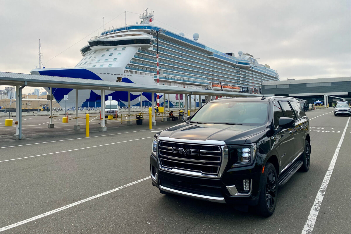 Black GMC SUV parked at the Seattle cruise terminal with a large cruise ship at the dock.