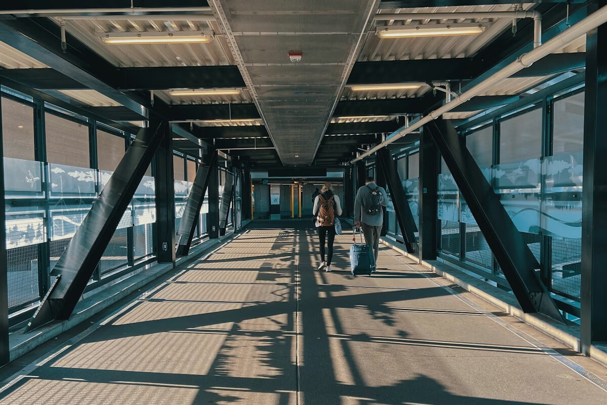 Travelers walking through the Sea-Tac airport skybridge corridor toward ground transportation, pulling rolling luggage.