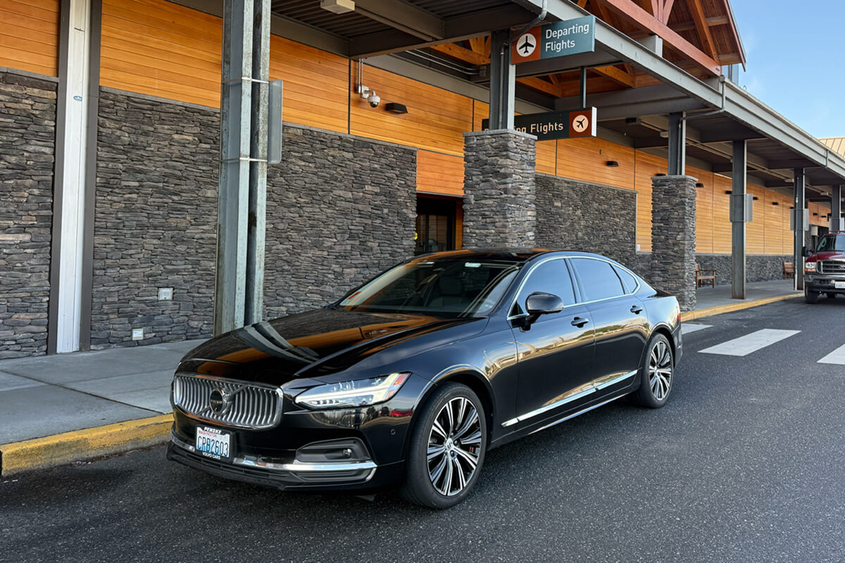 Black Volvo sedan at the Bellingham International Airport departures curb for private airport transportation.
