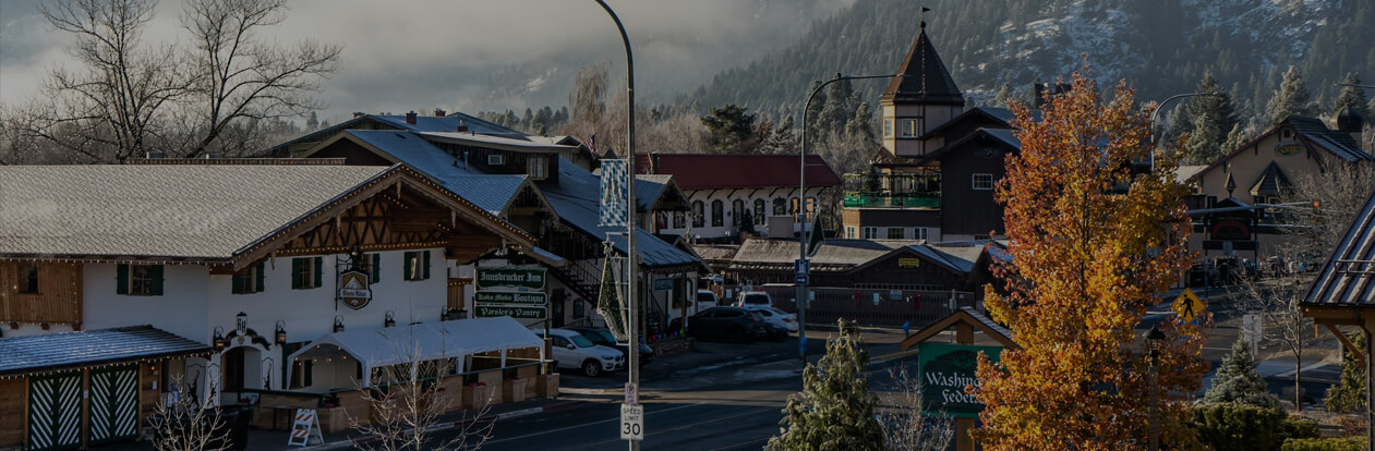 Autumn view of downtown Leavenworth with alpine-style buildings, a golden tree, and snow-dusted Cascade mountains in the background