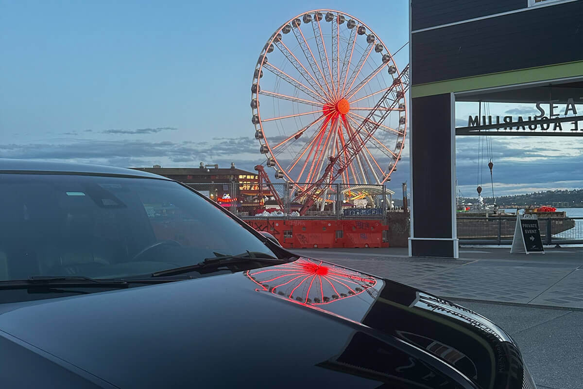 Black luxury SUV parked near Seattle waterfront with the Seattle Great Wheel glowing at dusk