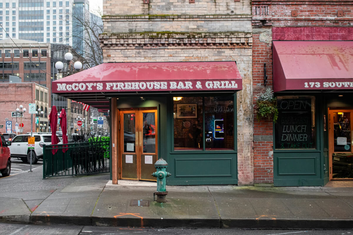 McCoy’s Firehouse Bar & Grill in Seattle’s Pioneer Square district, with its red awning, brick façade, and street activity on a rainy day.