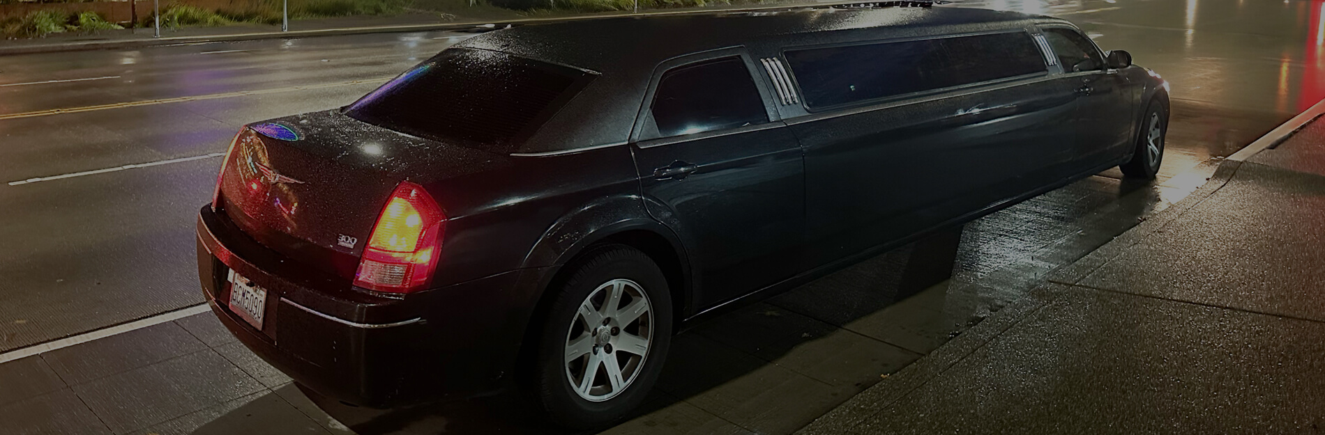Black stretch limousine parked at the curb on a wet Seattle street at night for private event transportation