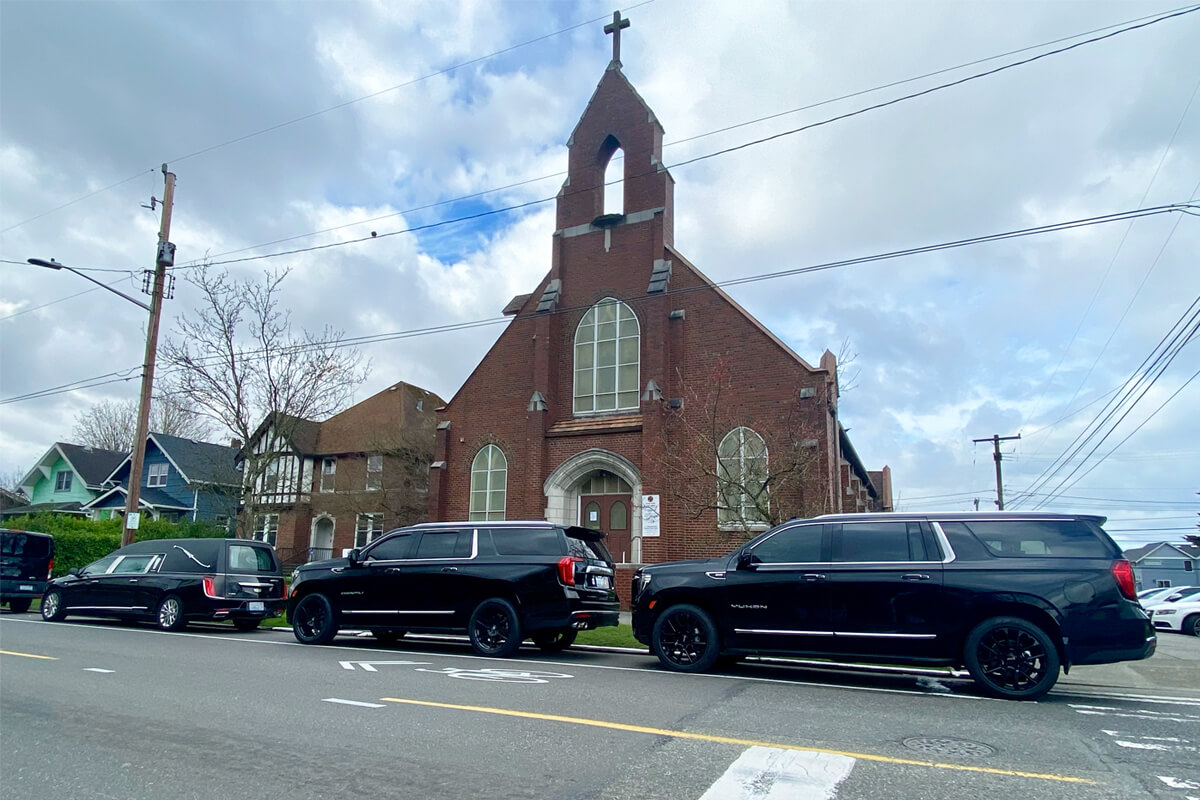 Hearse and black SUVs parked outside a brick church for funeral transportation service in Seattle