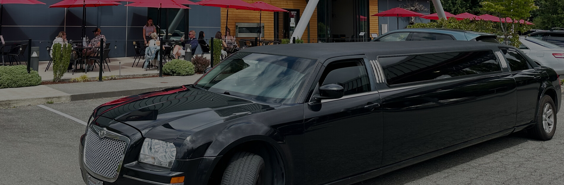 Black stretch limo parked outside a modern winery tasting room patio with red umbrellas during a private wine tour outing