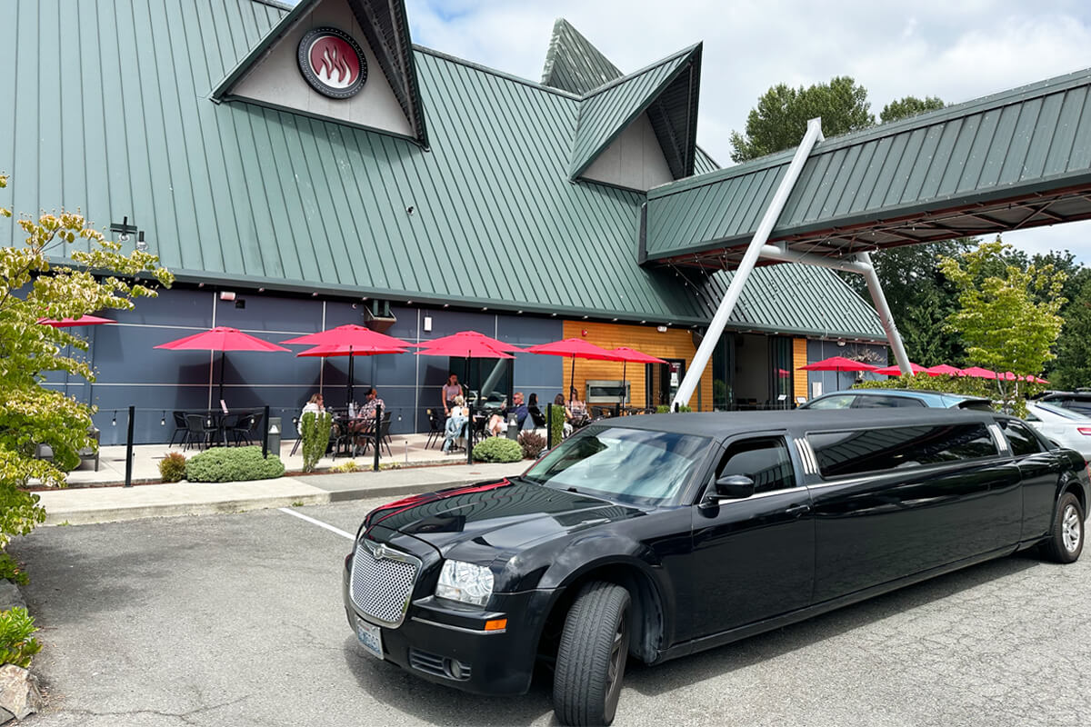 Black stretch limo parked outside a winery patio with red umbrellas during a private wine tasting trip