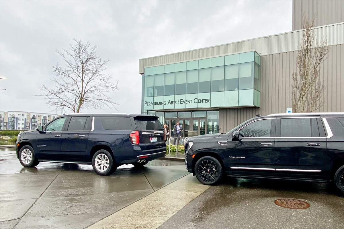 Two black SUVs parked outside a performing arts and event center for coordinated business event transportation
