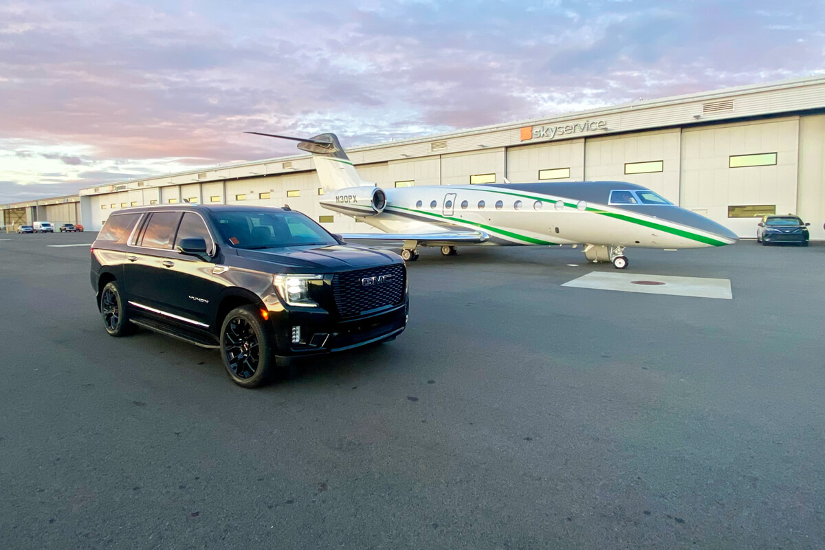 Black GMC Yukon beside a private jet outside a Skyservice hangar