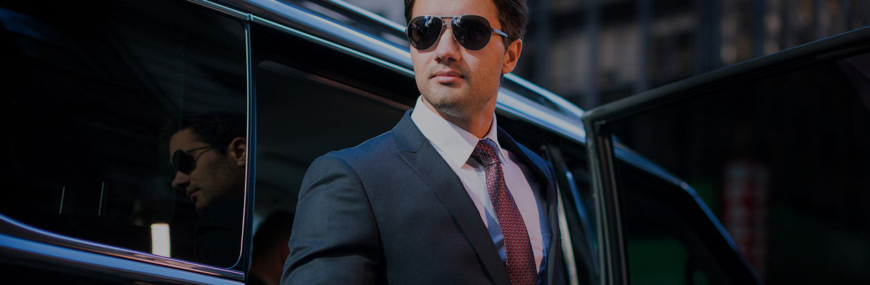Professional chauffeur beside a black private car